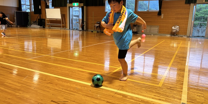 体育館でサッカーボールを蹴る小学生